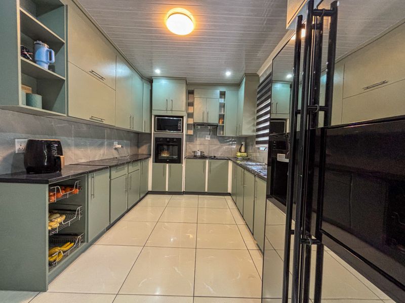 A modern, well-maintained kitchen featuring sage green cabinetry, stone countertops, tiled flooring, and integrated appliances including an oven and microwave.