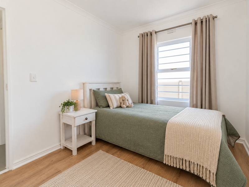 A well-maintained bedroom featuring light wood-look laminate flooring, neutral walls, and a window with fitted curtain hardware.