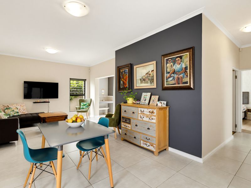 An open-plan living and dining area featuring neutral tiled flooring, a dark grey feature wall, and coved cornicing throughout the space.