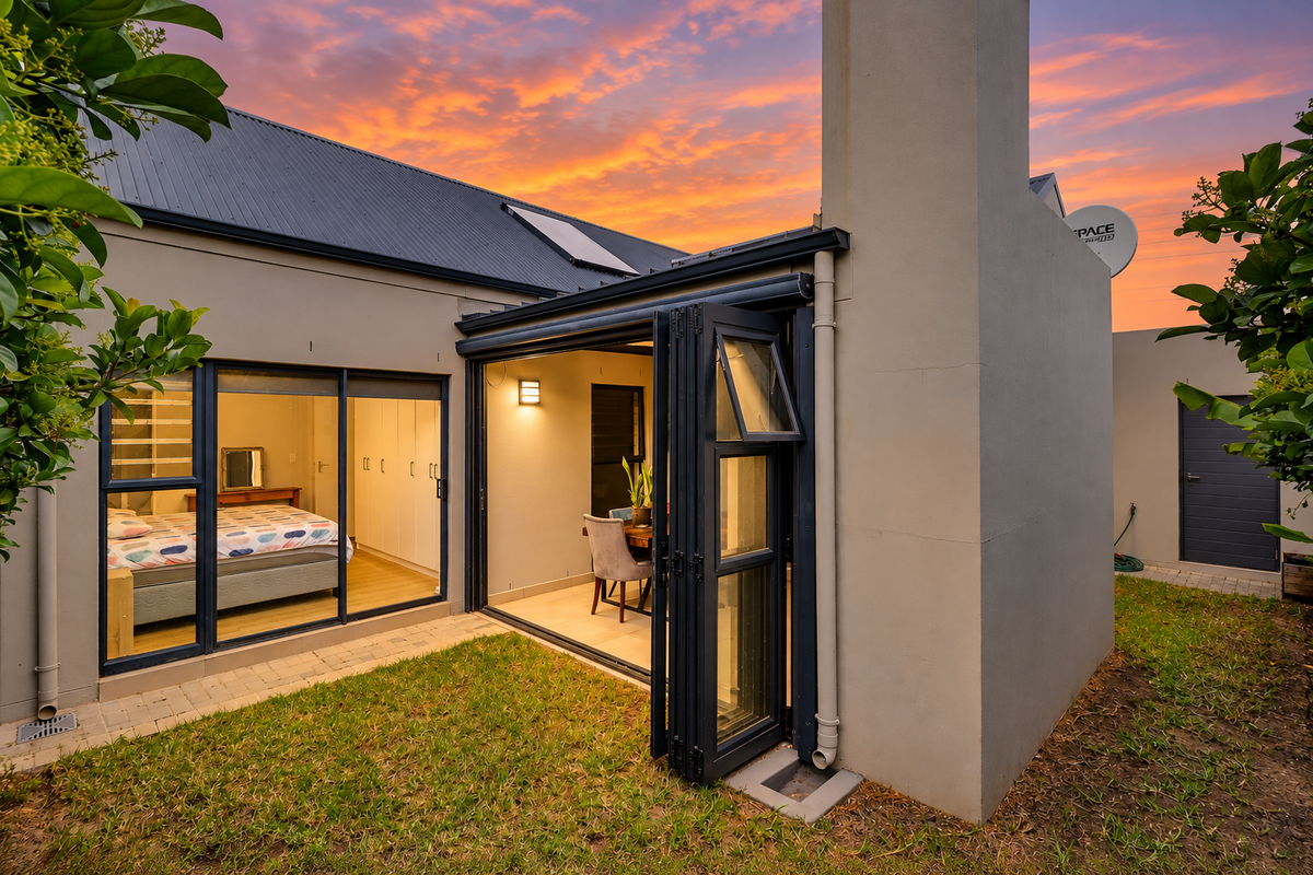 Rear view of the property featuring a modern exterior with bi-fold doors, a prominent chimney, and a well-maintained garden area at sunset.