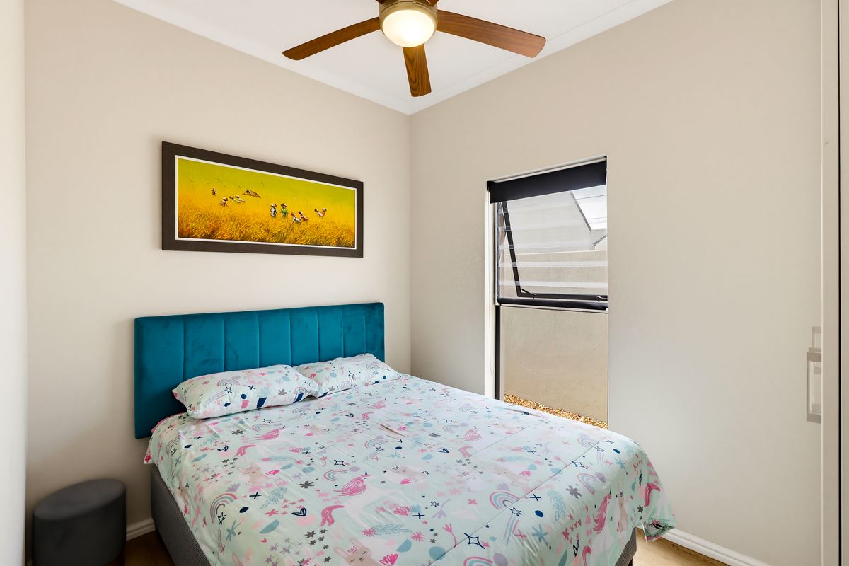 A well-maintained bedroom featuring a ceiling fan, louver window, and built-in wardrobe, offering a clean and functional living space.