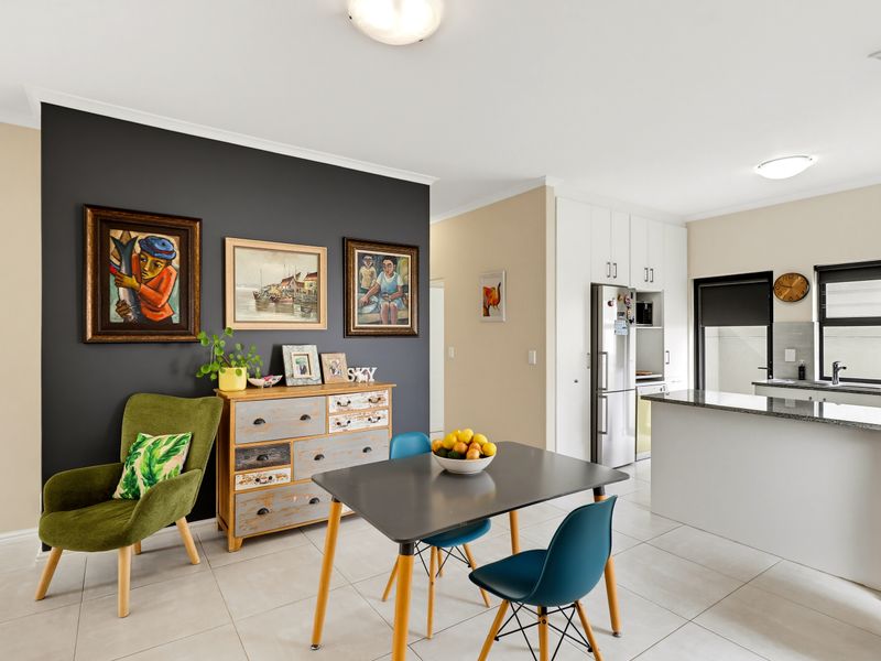 Bright open-plan living and kitchen area featuring modern tiled flooring, sleek granite countertops, and a striking dark feature wall.