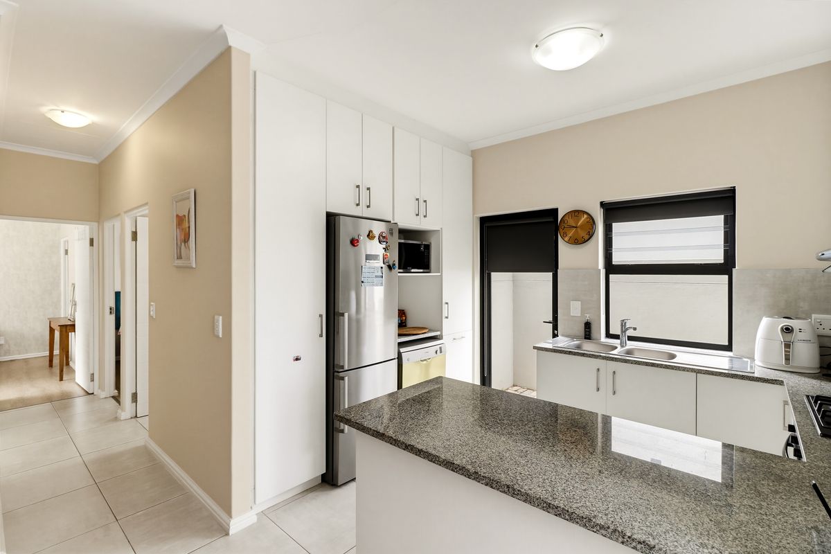 A functional kitchen featuring granite countertops, ample built-in cabinetry, and a double basin sink, with direct access to an adjacent hallway.