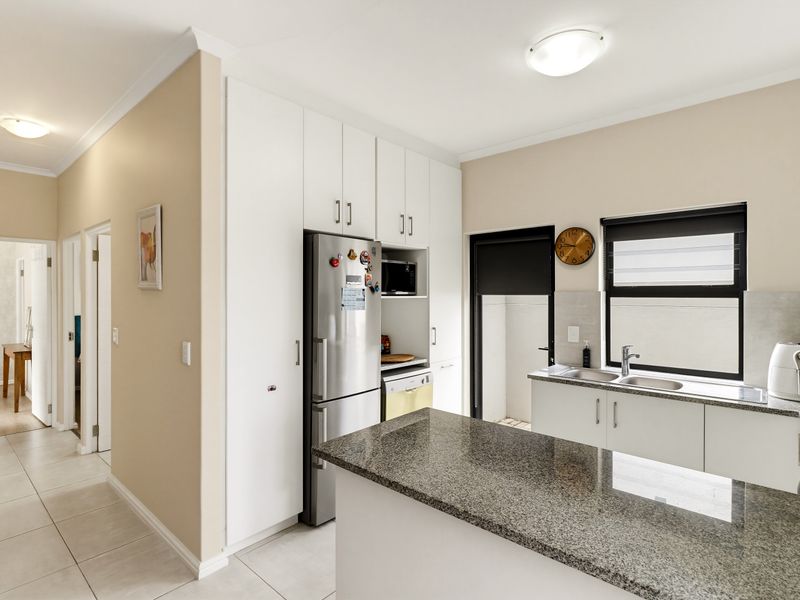 A functional kitchen featuring granite countertops, ample built-in cabinetry, and a double basin sink, with direct access to an adjacent hallway.