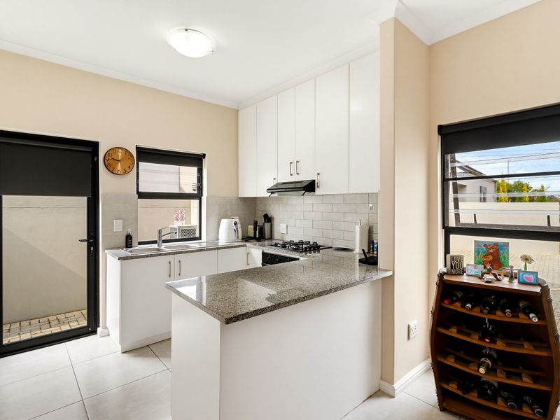 A modern, well-maintained kitchen featuring white cabinetry, granite countertops, a gas hob, and a stylish subway tile backsplash with direct outdoor access.