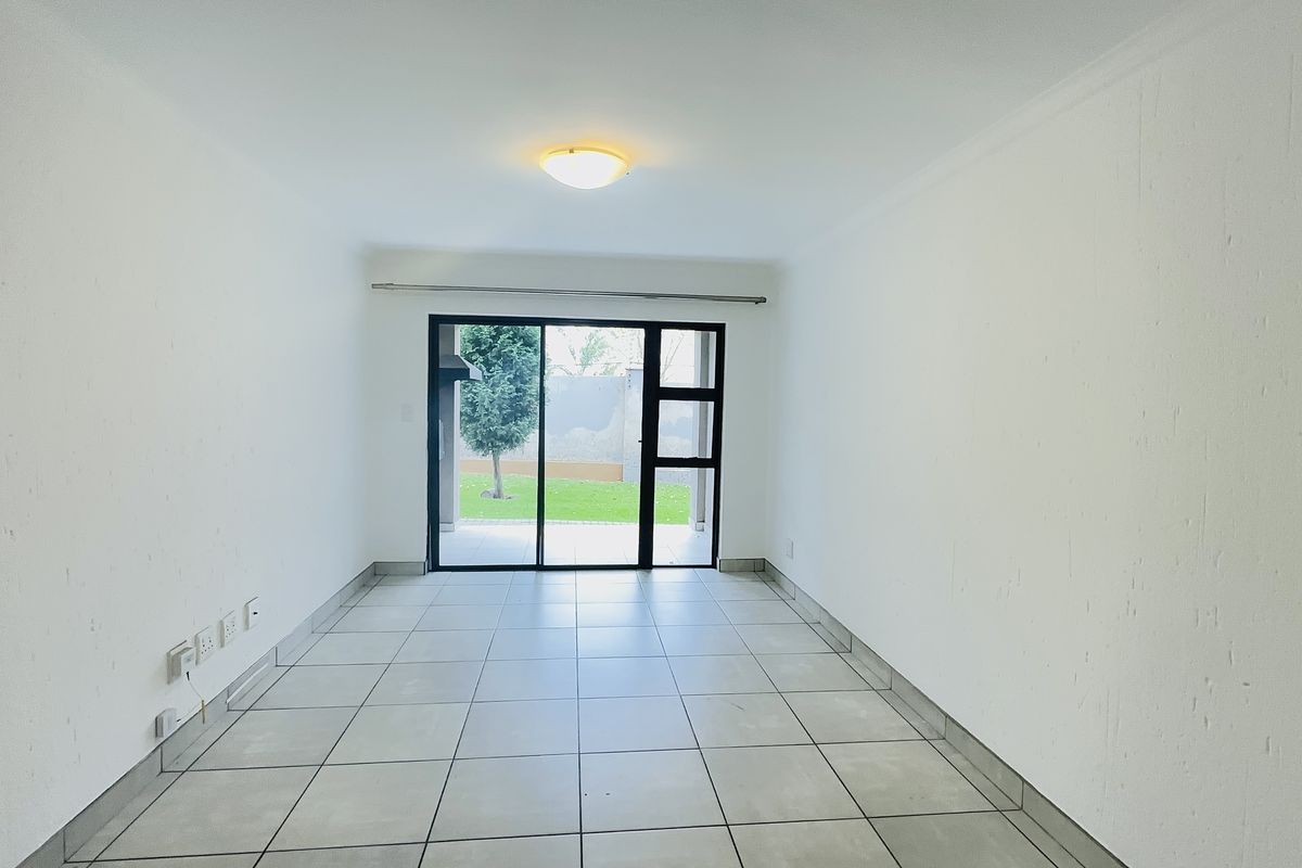 A bright, empty living room featuring neutral tiled flooring and a large sliding glass door providing access to the outdoor area.