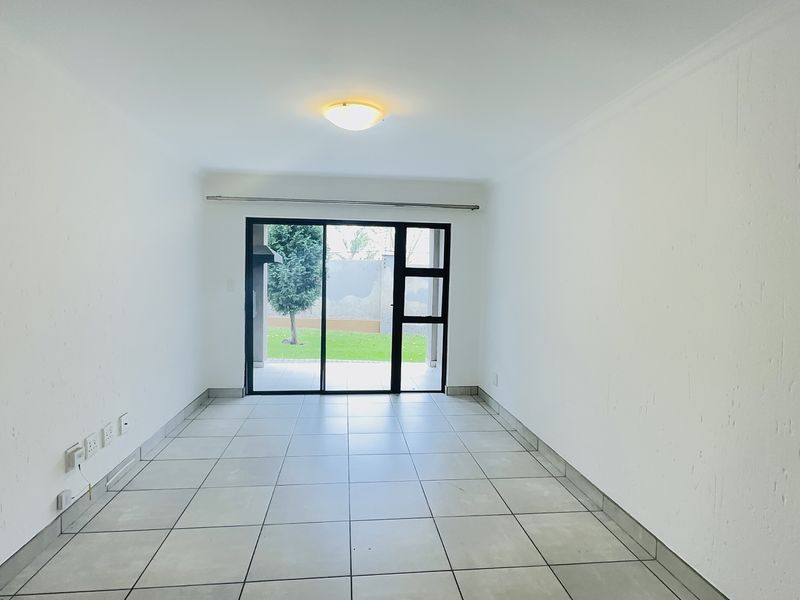 A bright, empty living room featuring neutral tiled flooring and a large sliding glass door providing access to the outdoor area.