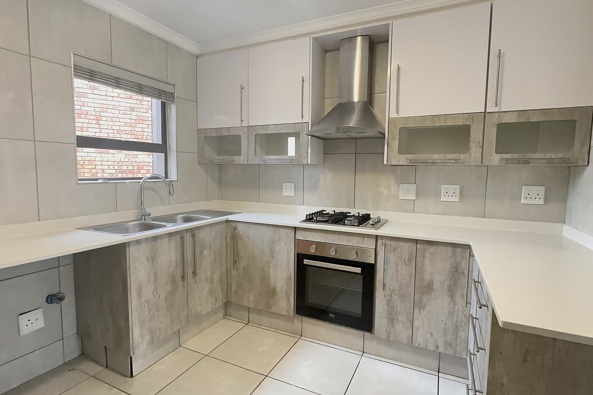 Modern kitchen featuring stone countertops, built-in oven, gas hob, extractor fan, and ample cabinetry with a neutral tiled finish.