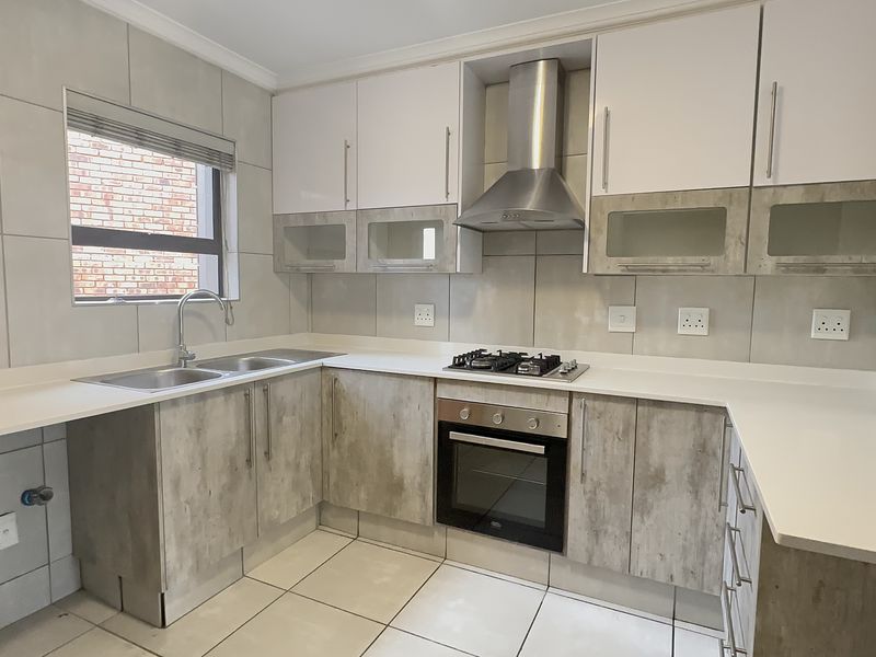 Modern kitchen featuring stone countertops, built-in oven, gas hob, extractor fan, and ample cabinetry with a neutral tiled finish.