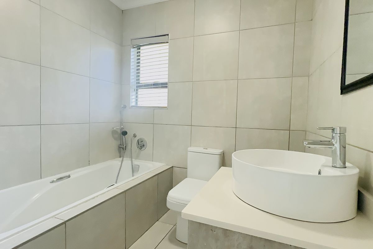 A clean, modern bathroom featuring a built-in bathtub, a contemporary vessel sink on a vanity countertop, and neutral floor-to-ceiling wall tiles.