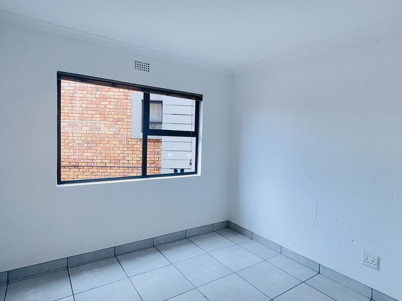 A clean, empty bedroom featuring neutral tiled flooring, a large aluminium-framed window, and simple white walls, ready for personalization.
