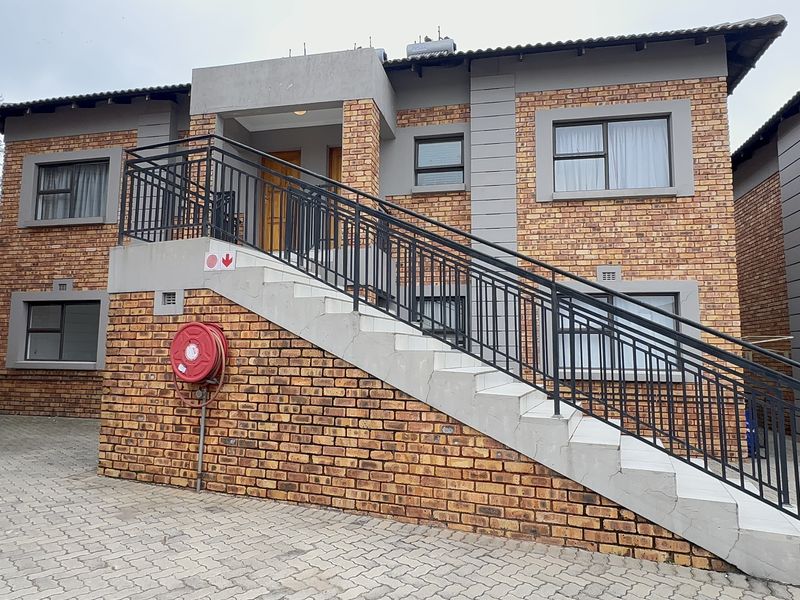 Exterior view of a face brick apartment building featuring an external staircase with metal balustrades and paved driveway access.