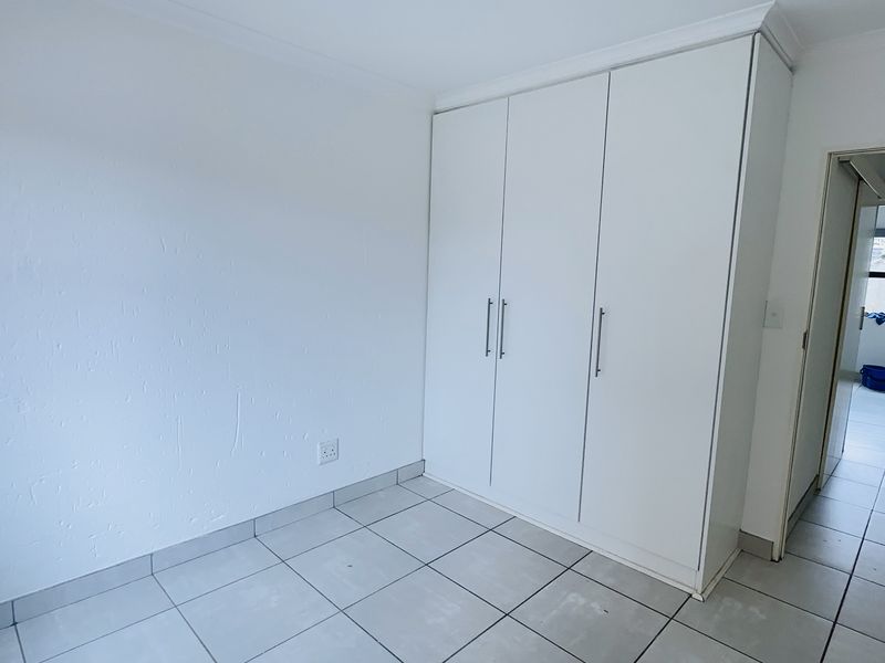 A clean, empty bedroom featuring neutral tiled flooring and white built-in cupboards, offering a bright and versatile space.