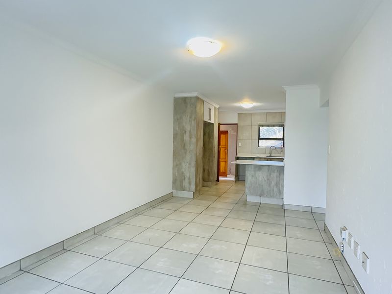 An open-plan living and kitchen area featuring neutral tiled flooring, modern cabinetry, and a breakfast bar, offering a clean and versatile space.