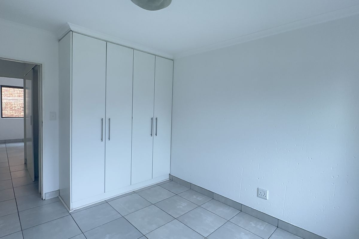 A clean, empty bedroom featuring neutral tiled flooring and white built-in cupboards, offering a blank canvas for personalization.