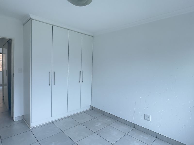 A clean, empty bedroom featuring neutral tiled flooring and white built-in cupboards, offering a blank canvas for personalization.