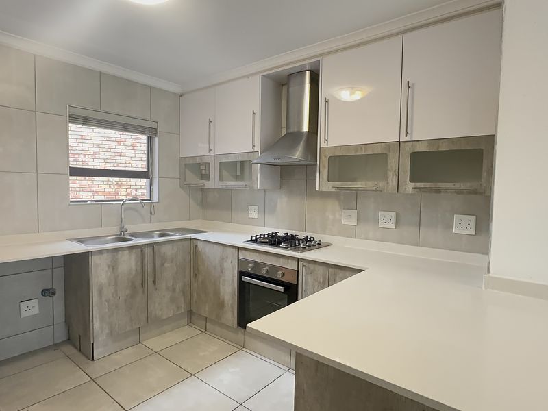 A modern, well-maintained kitchen featuring stone countertops, built-in cabinetry, a gas hob, and an integrated oven with a stainless steel extractor fan.