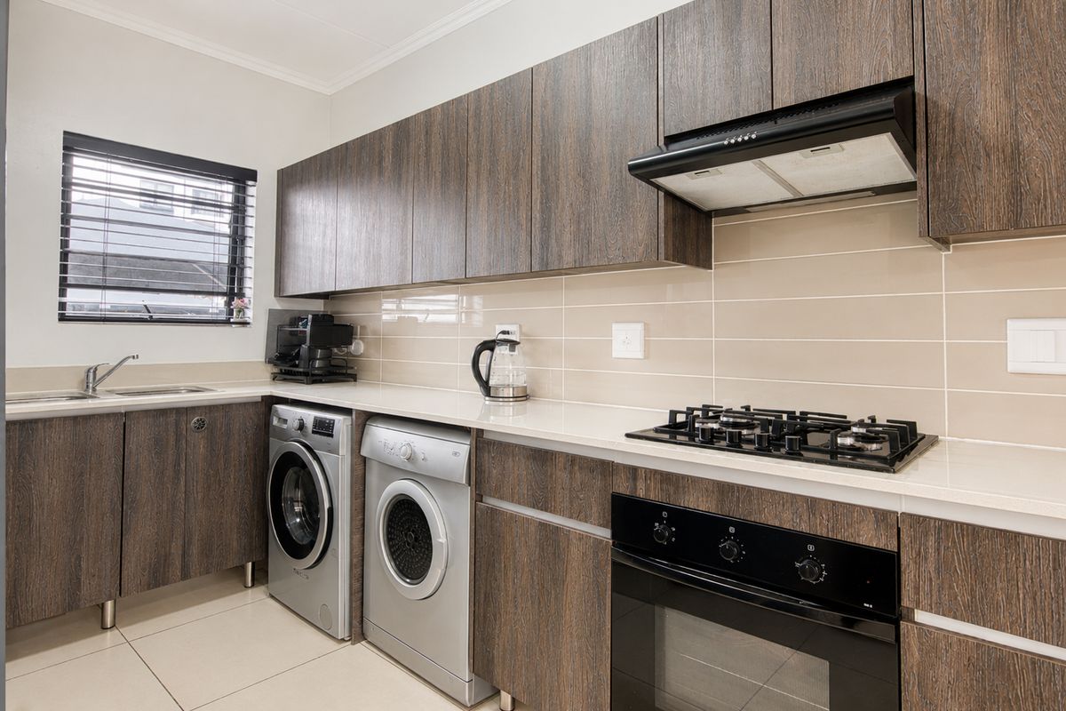 Modern kitchen featuring dark wood cabinetry, stone countertops, gas hob, integrated oven, extractor fan, and dedicated space for laundry appliances.