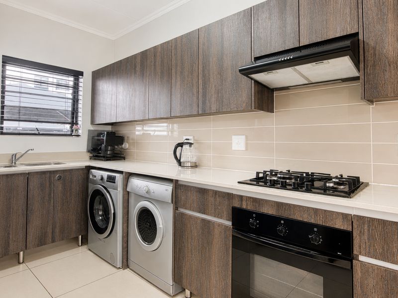 Modern kitchen featuring dark wood cabinetry, stone countertops, gas hob, integrated oven, extractor fan, and dedicated space for laundry appliances.