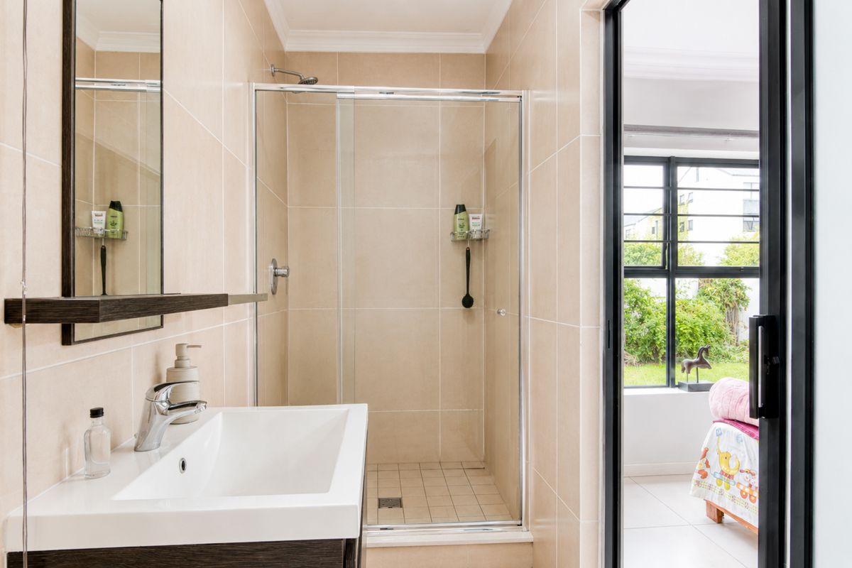 A modern bathroom featuring a glass-enclosed shower, vanity basin with mixer tap, and neutral wall tiling, with direct access to an adjacent room.