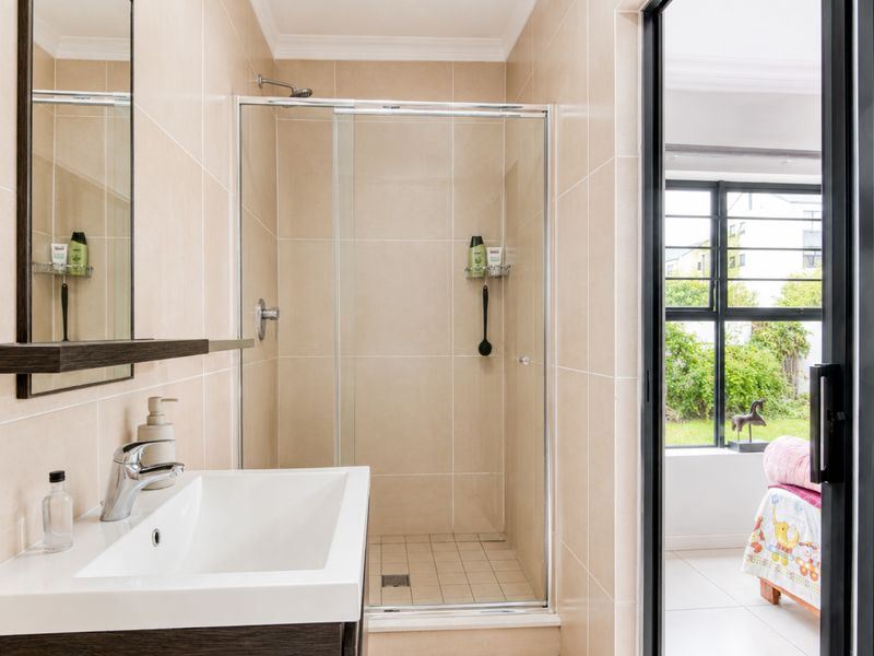 A modern bathroom featuring a glass-enclosed shower, vanity basin with mixer tap, and neutral wall tiling, with direct access to an adjacent room.