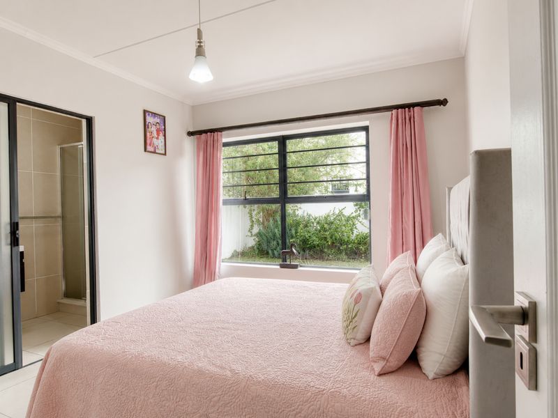 A well-maintained bedroom featuring an en-suite bathroom, large aluminium-framed window, and neutral finishes, offering a comfortable and functional living space.