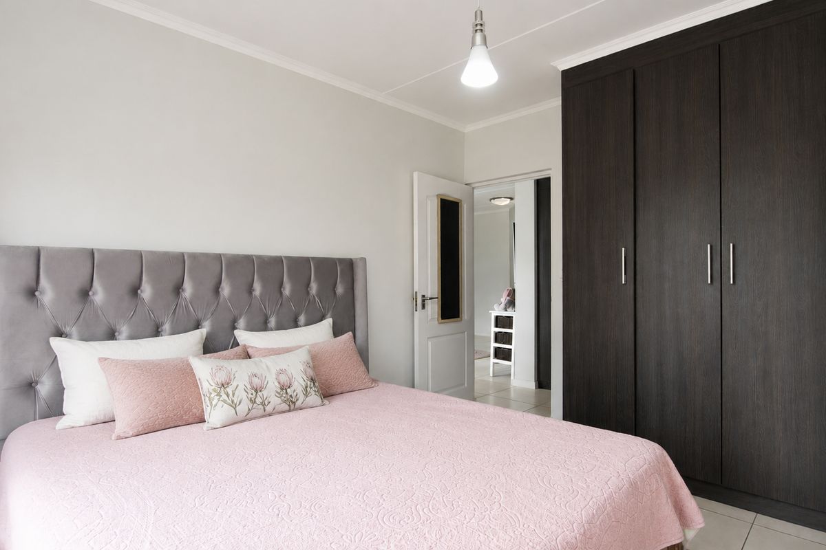 A well-maintained bedroom featuring a large dark wood built-in wardrobe, neutral walls, and tiled flooring, with a view into the adjacent hallway.