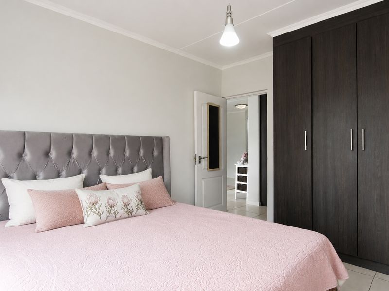 A well-maintained bedroom featuring a large dark wood built-in wardrobe, neutral walls, and tiled flooring, with a view into the adjacent hallway.