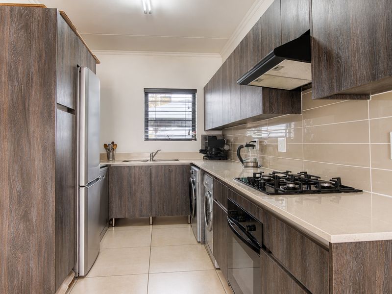 Modern galley-style kitchen featuring dark wood-grain cabinetry, stone countertops, gas hob, integrated oven, and tiled splashback with ample storage space.