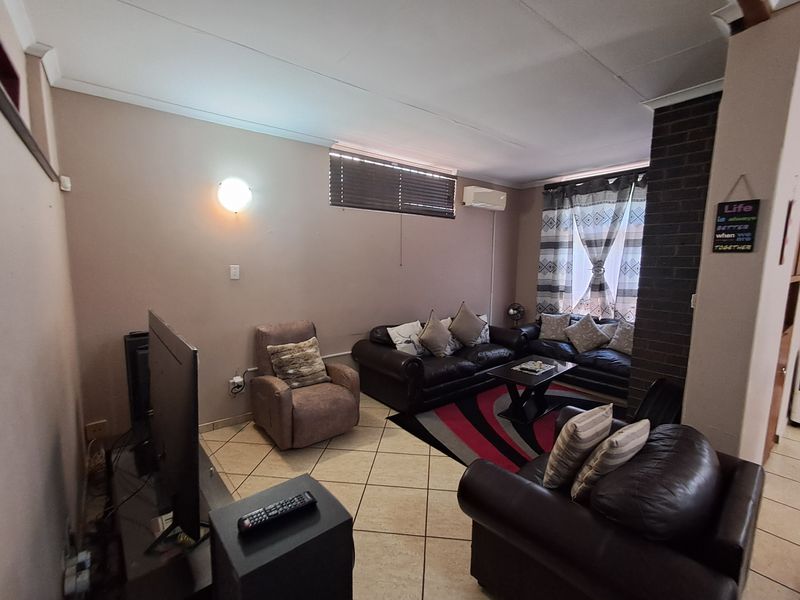 A comfortable living room featuring tiled flooring, a brick feature wall, and a wall-mounted air conditioning unit.