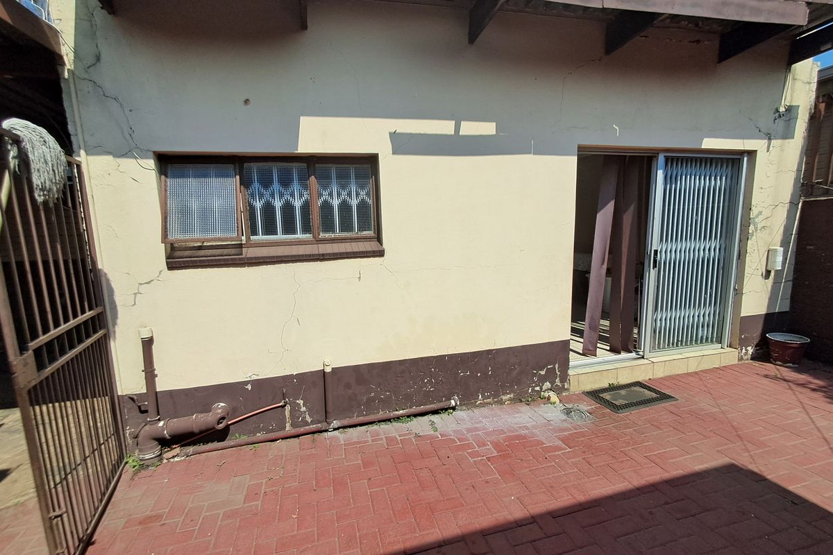 Rear exterior view showing a paved patio area, sliding door access, and visible wear to the exterior wall plaster and paintwork.