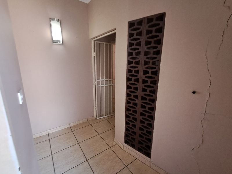 An entry area featuring tiled flooring, a decorative breeze block screen, and a security gate, currently showing a significant vertical wall crack.