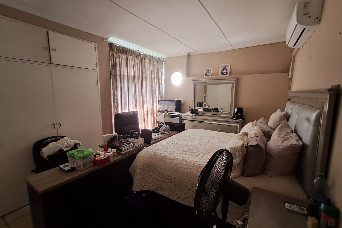 A bedroom featuring built-in cupboards, tiled flooring, and a wall-mounted air conditioning unit.