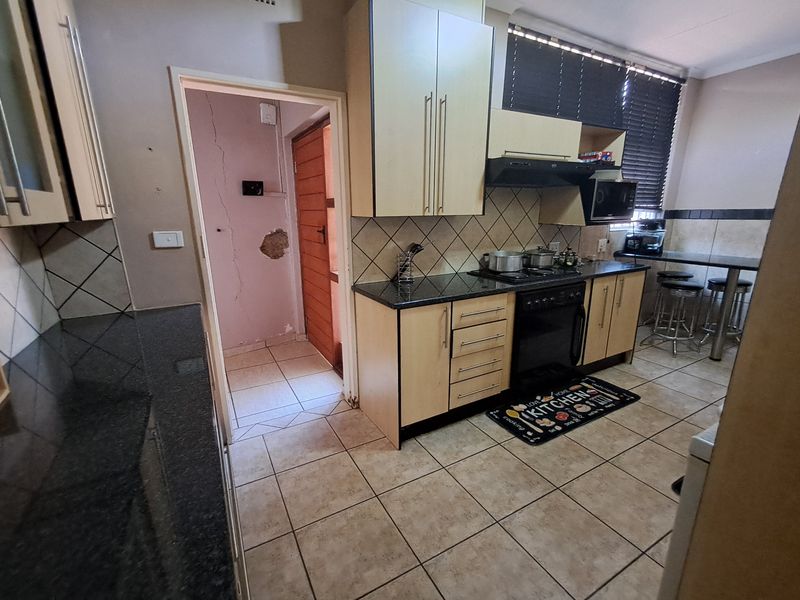 Functional kitchen featuring granite countertops, built-in cabinetry, gas hob, and an integrated breakfast bar, with an adjacent utility area showing some wall damage.