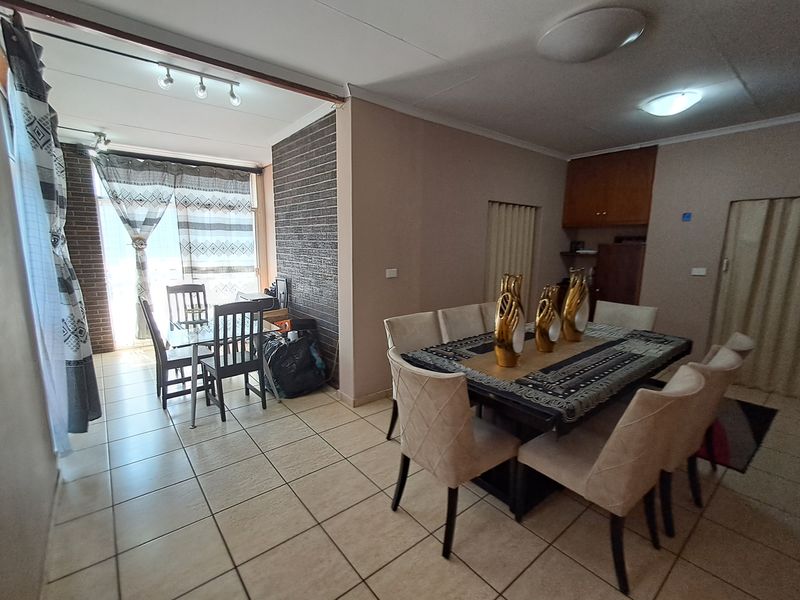 Open plan living and dining area featuring tiled flooring, a brick feature wall, and integrated ceiling lighting, offering a functional and versatile living space.