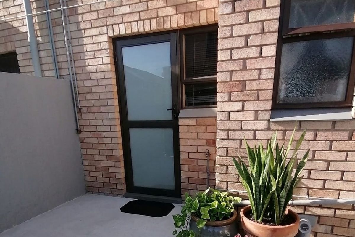 A rear exterior view of the townhouse featuring a face brick facade, concrete patio area, and a frosted glass door.