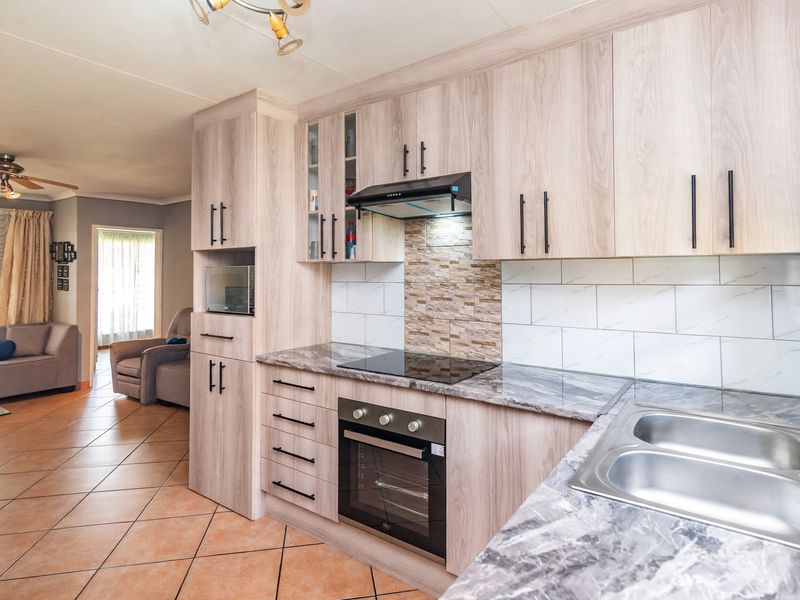 Modern open-plan kitchen featuring light wood-grain cabinetry, marble-effect countertops, integrated appliances, and a tiled backsplash, seamlessly flowing into the adjacent living area.