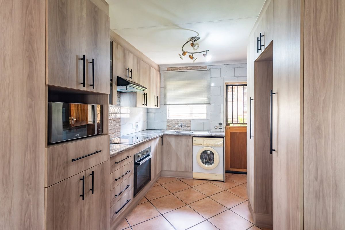 Modern kitchen featuring wood-look cabinetry, integrated appliances, tiled backsplash, and durable tiled flooring with direct access to the exterior.