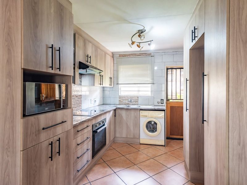 Modern kitchen featuring wood-look cabinetry, integrated appliances, tiled backsplash, and durable tiled flooring with direct access to the exterior.
