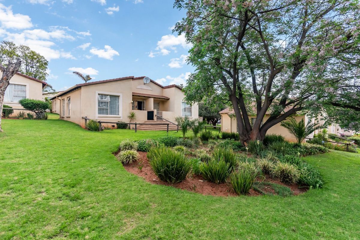 A well-maintained townhouse exterior featuring a landscaped garden, mature trees, and a tiled roof, showcasing the property's rear elevation and outdoor space.