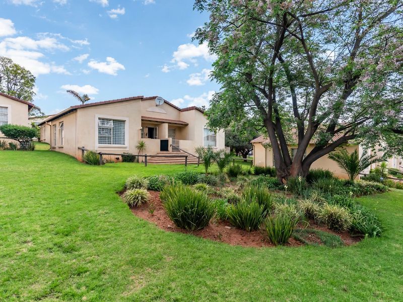 A well-maintained townhouse exterior featuring a landscaped garden, mature trees, and a tiled roof, showcasing the property's rear elevation and outdoor space.