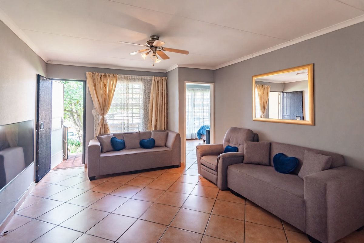 Spacious living room featuring ceramic tiled flooring, a ceiling fan, and direct access to the exterior through a security gate.