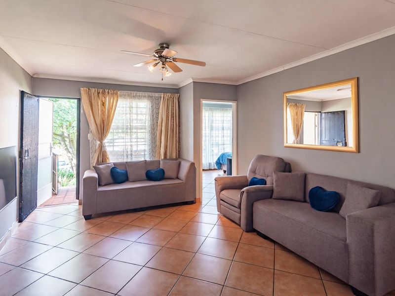 Spacious living room featuring ceramic tiled flooring, a ceiling fan, and direct access to the exterior through a security gate.