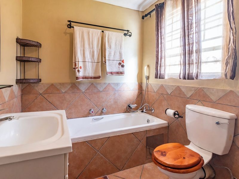 A functional bathroom featuring a built-in bathtub, vanity basin, and toilet, finished with traditional ceramic wall and floor tiling.