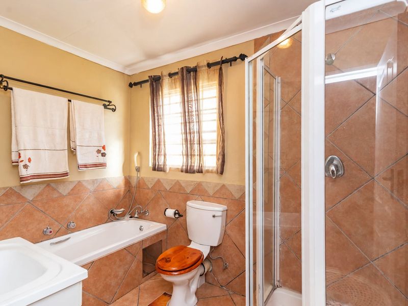 A functional bathroom featuring a built-in bathtub, separate shower enclosure, toilet, and vanity basin with neutral tiled finishes.