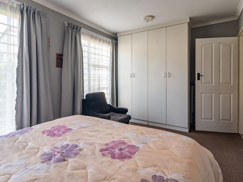 A functional bedroom featuring built-in cupboards, carpeted flooring, and large windows with security bars, offering a comfortable and practical living space.