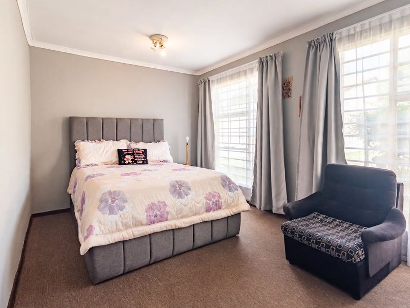A well-lit bedroom featuring neutral wall tones, carpeted flooring, and large windows fitted with security bars.