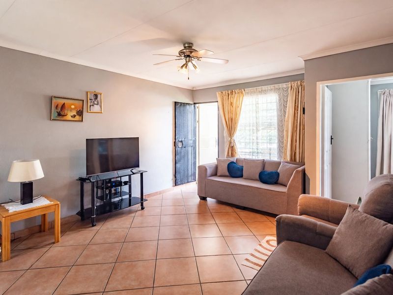 A functional living room featuring ceramic floor tiles, a ceiling fan, and direct access to an exterior security gate.