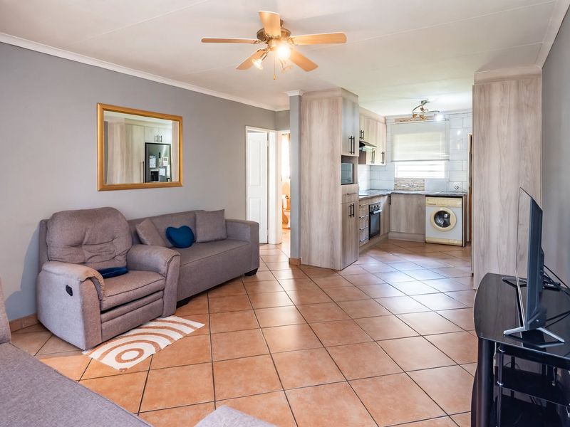 Open-plan living area featuring tiled flooring, a ceiling fan, and a functional kitchen with built-in cabinetry, oven, and extractor fan.