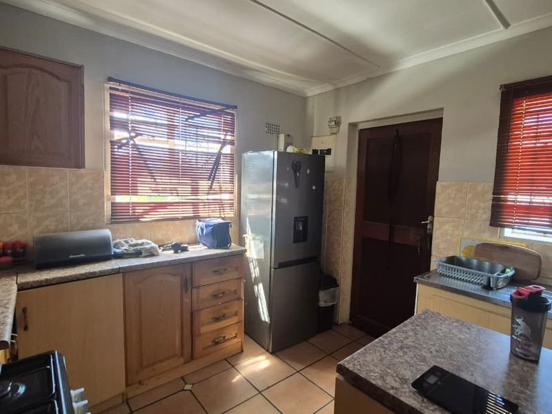A functional kitchen featuring laminate cabinetry, tiled backsplash, and tiled flooring, offering a practical layout with ample counter space and natural light.